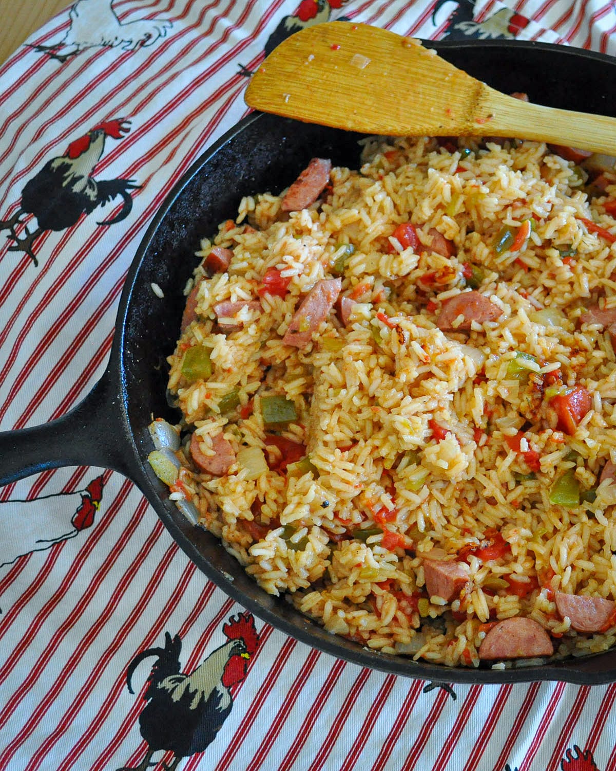 a cast iron skillet filled with jambalaya sitting on a rooster print apron