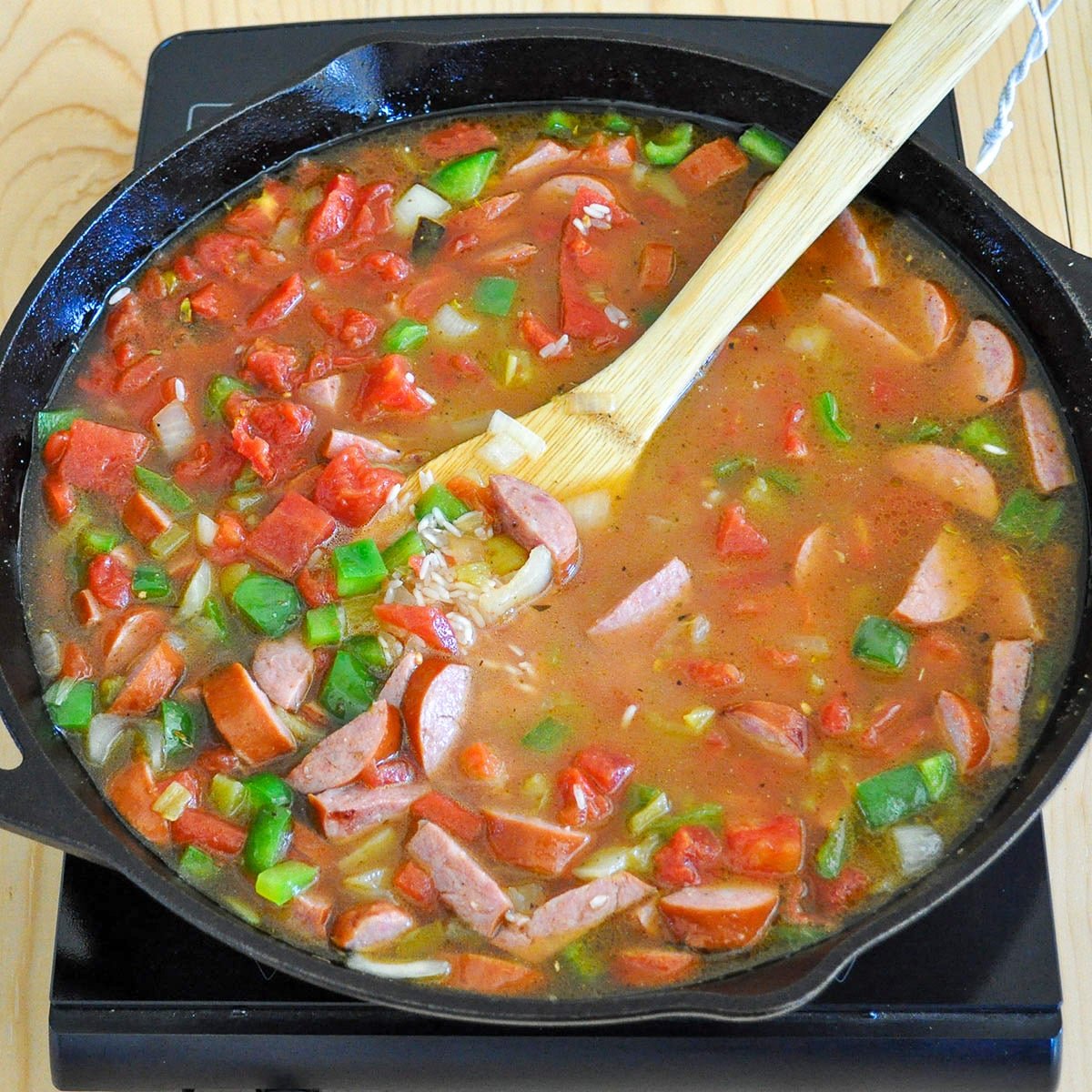 A cast iron skillet with jambalaya ingredients ready to cover to cook the rice. 