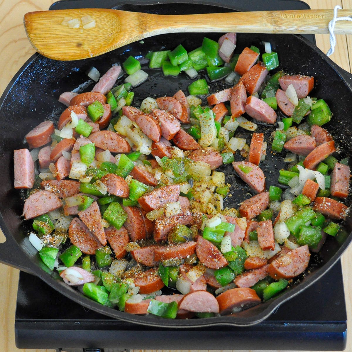 seasoning added to sausage, onion, and bell pepper cooking in a cast iron skillet