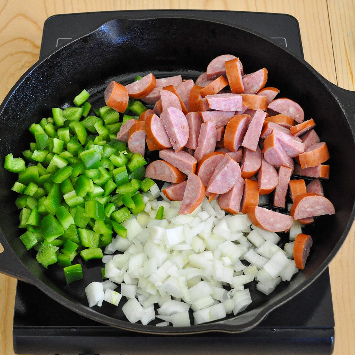 a cast iron skillet on a burner filled with onion, bell pepper, and sausage. 