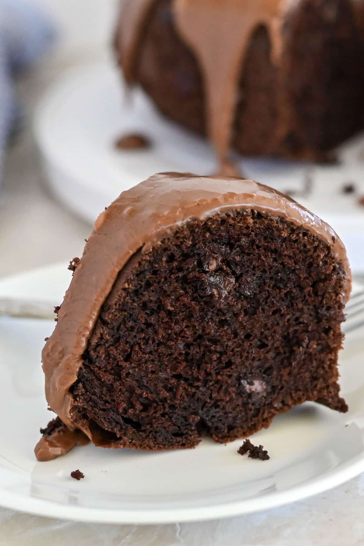 A slice of Chocolate Espresso Bundt Cake with rich chocolate glaze sits elegantly on a white plate.