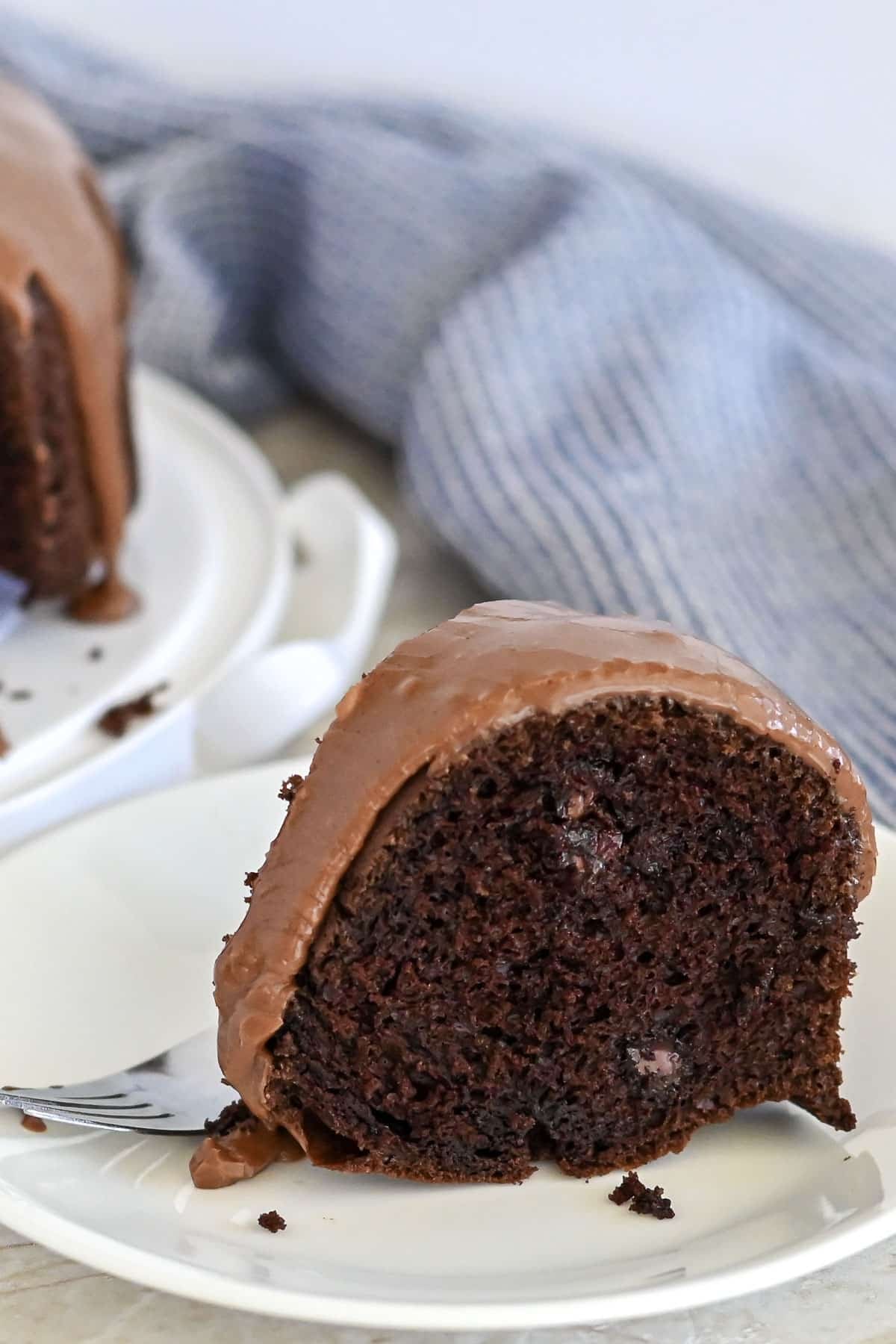 A slice of moist Chocolate Espresso Bundt Cake with rich chocolate icing on a white plate, fork beside it.