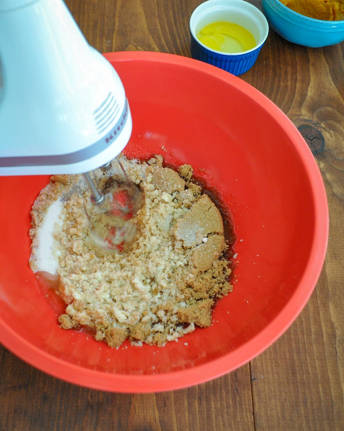 brown and white sugars being beaten with an electric mixer in a large red bowl 
