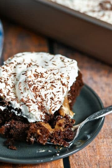 A square piece of chocolate cake covered with pudding and whipped cream on a small gray plate.