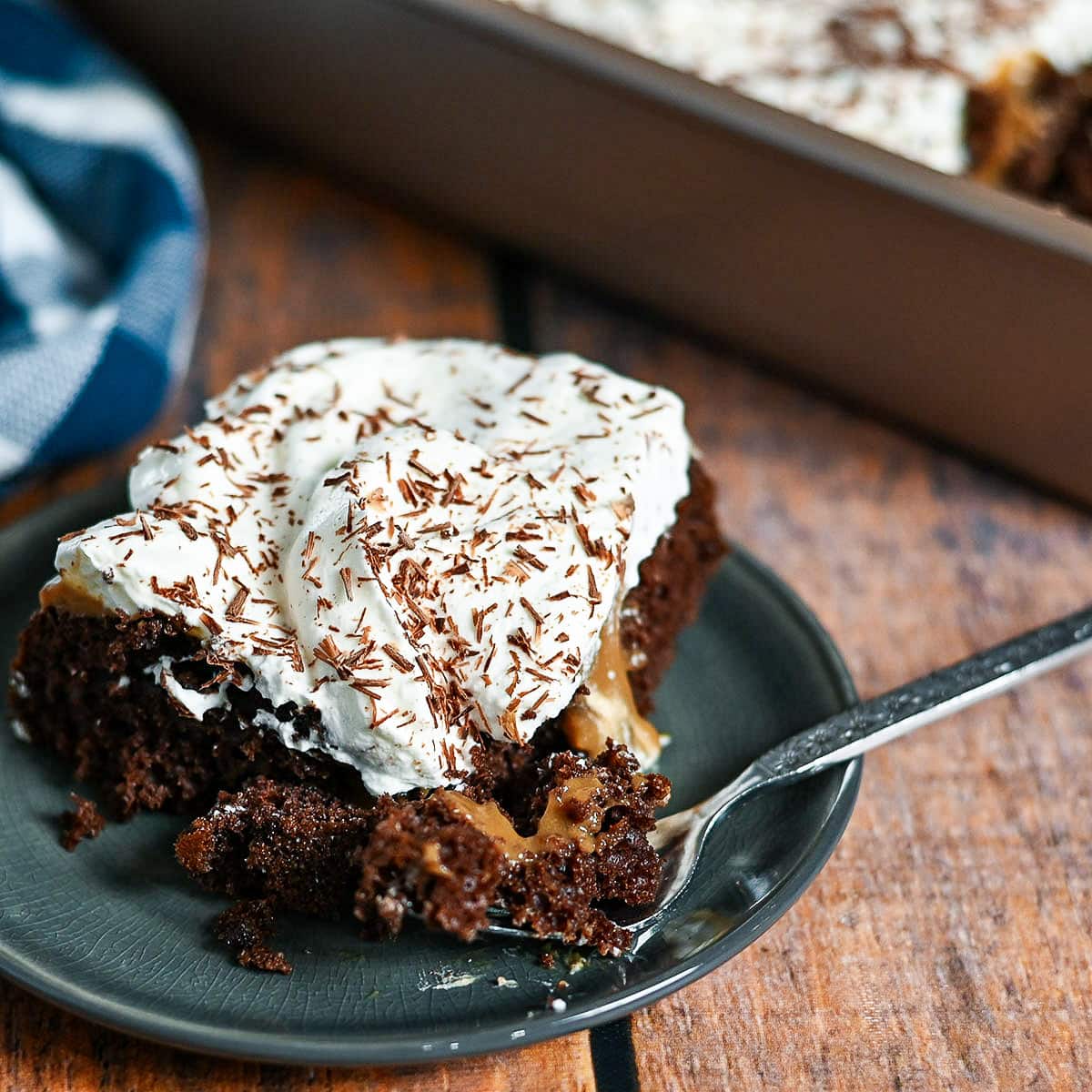 A square piece of chocolate cake covered with pudding and whipped cream on a small gray plate.