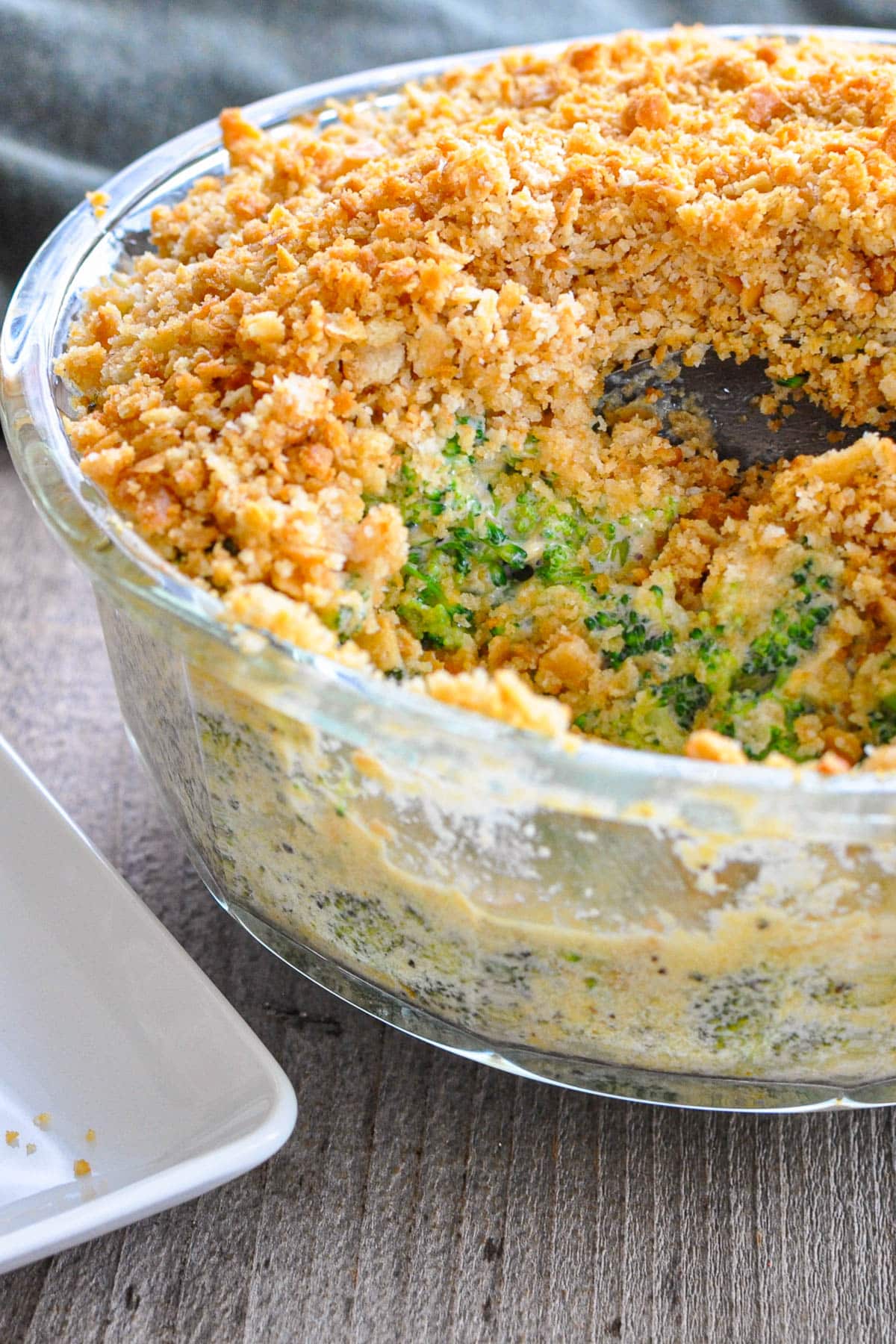 Glass dish of Simple Broccoli Casserole with a golden breadcrumb topping, partially scooped out with a spoon.