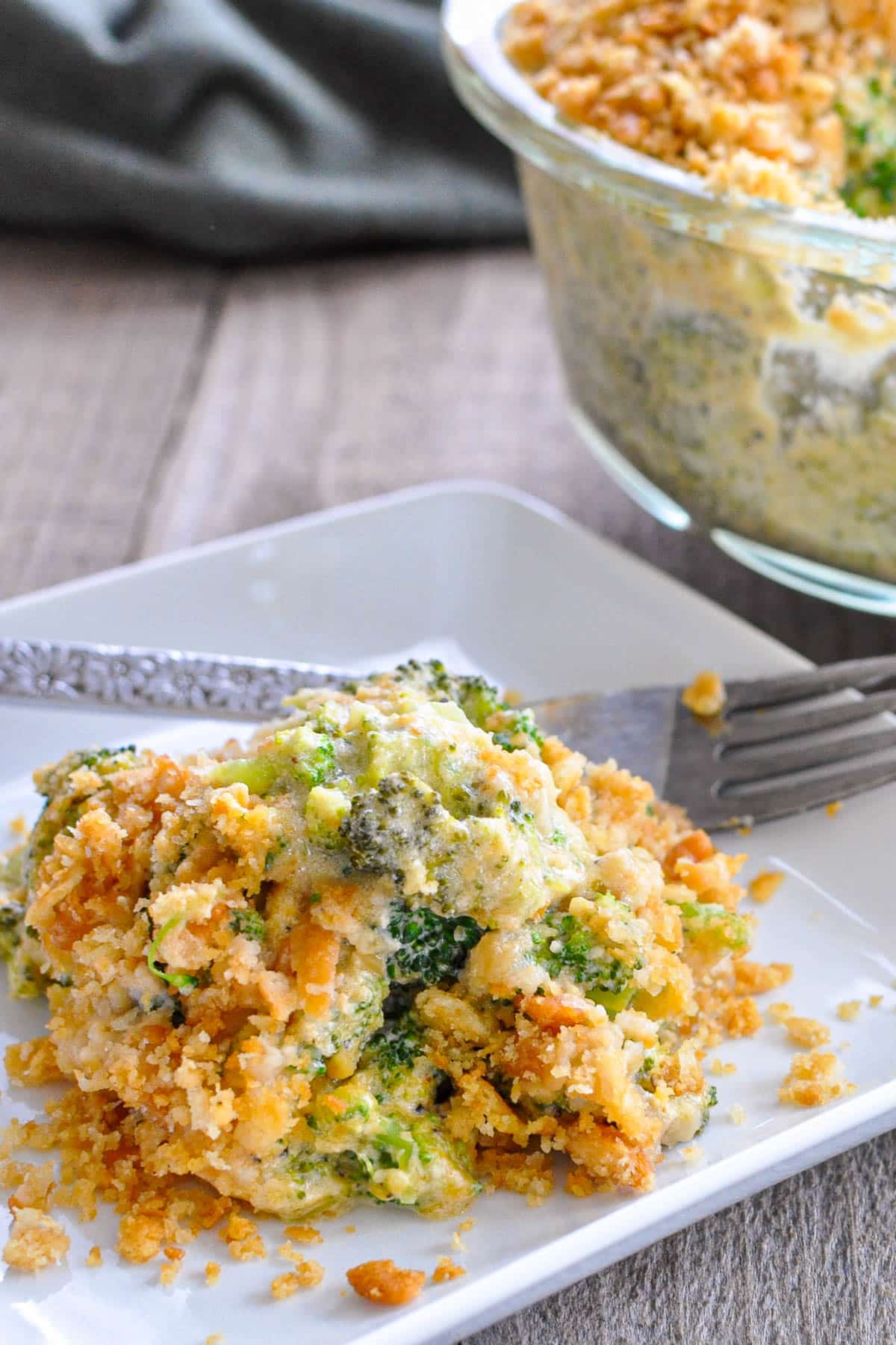 A serving of Simple Broccoli Casserole topped with crunchy crumbs sits on a white plate, with a fork beside it.