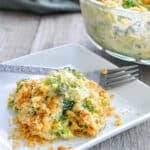Simple Broccoli Casserole with cheese and a crispy topping, served on a square white plate with a fork beside it.