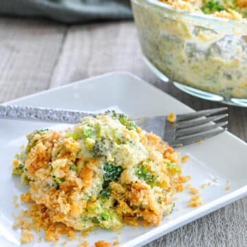 Simple Broccoli Casserole with cheese and a crispy topping, served on a square white plate with a fork beside it.