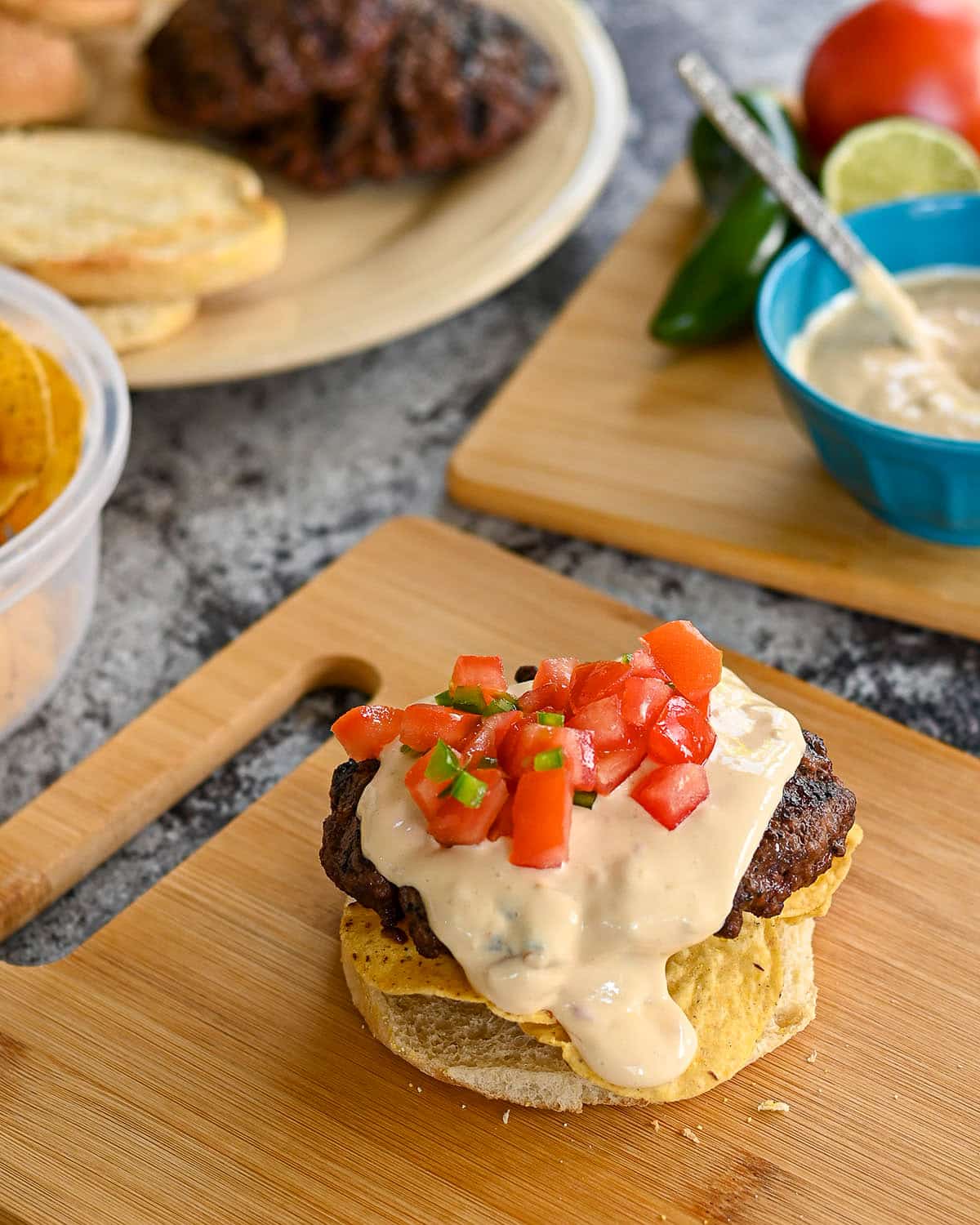 Queso cheese over a hamburger patty topped with tomato and jalapeno.