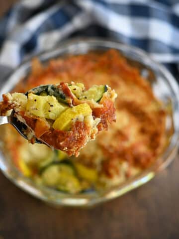 Baked squash with browned cheese in a clear bowl being served.