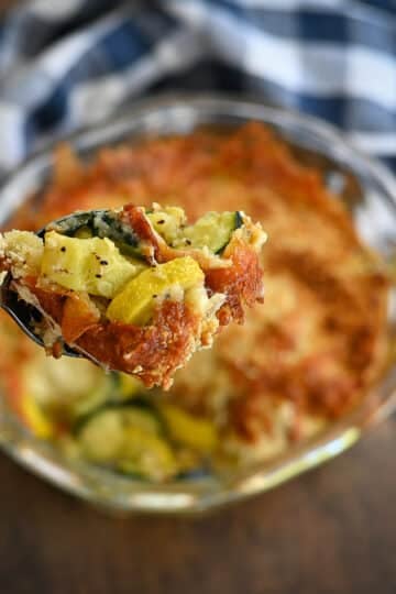 Baked squash with browned cheese in a clear bowl being served.