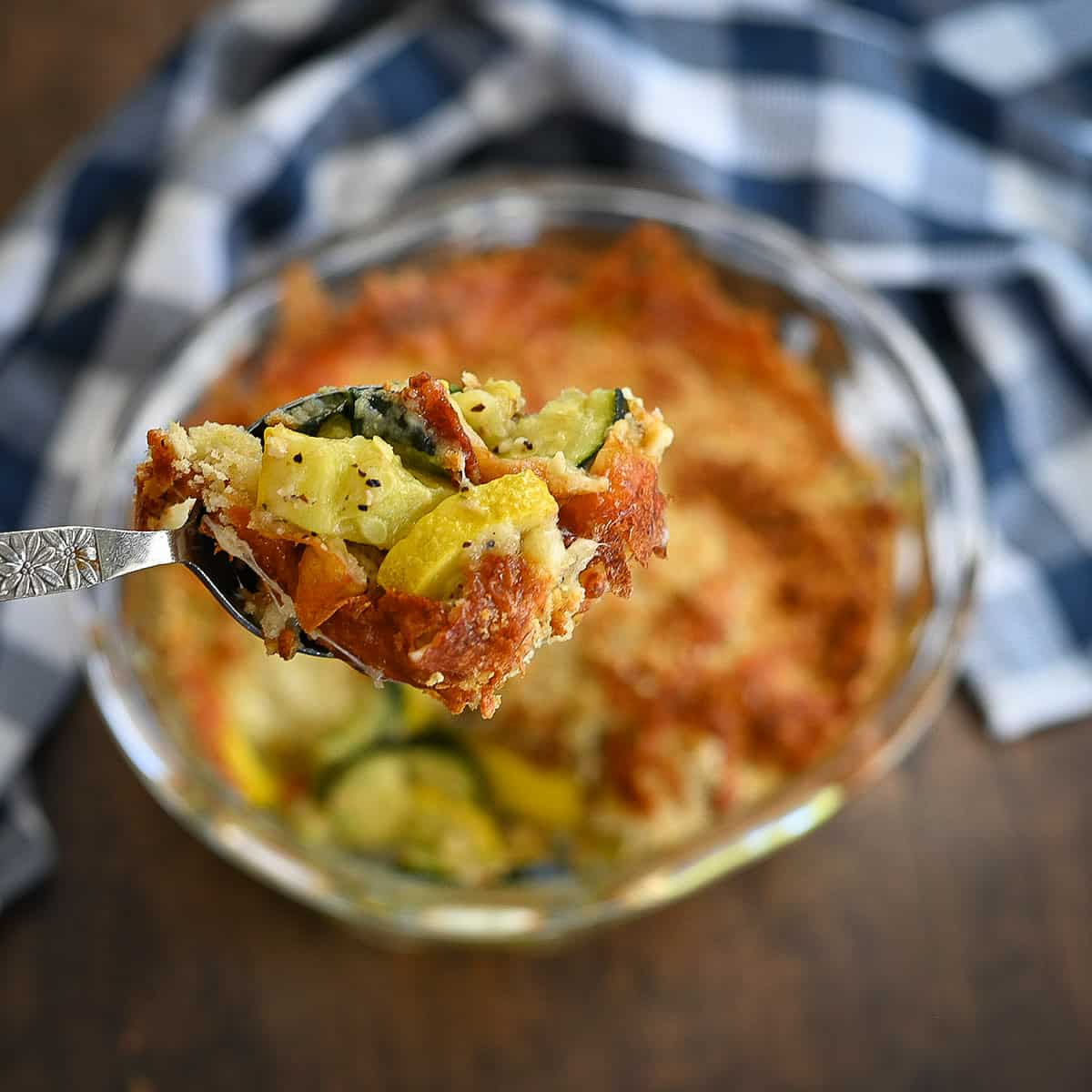 Baked squash with browned cheese in a clear bowl being served.