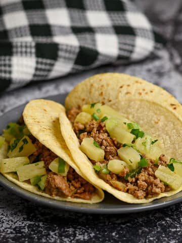 Three tortillas filled with ground meat and pineapple on a gray plate.
