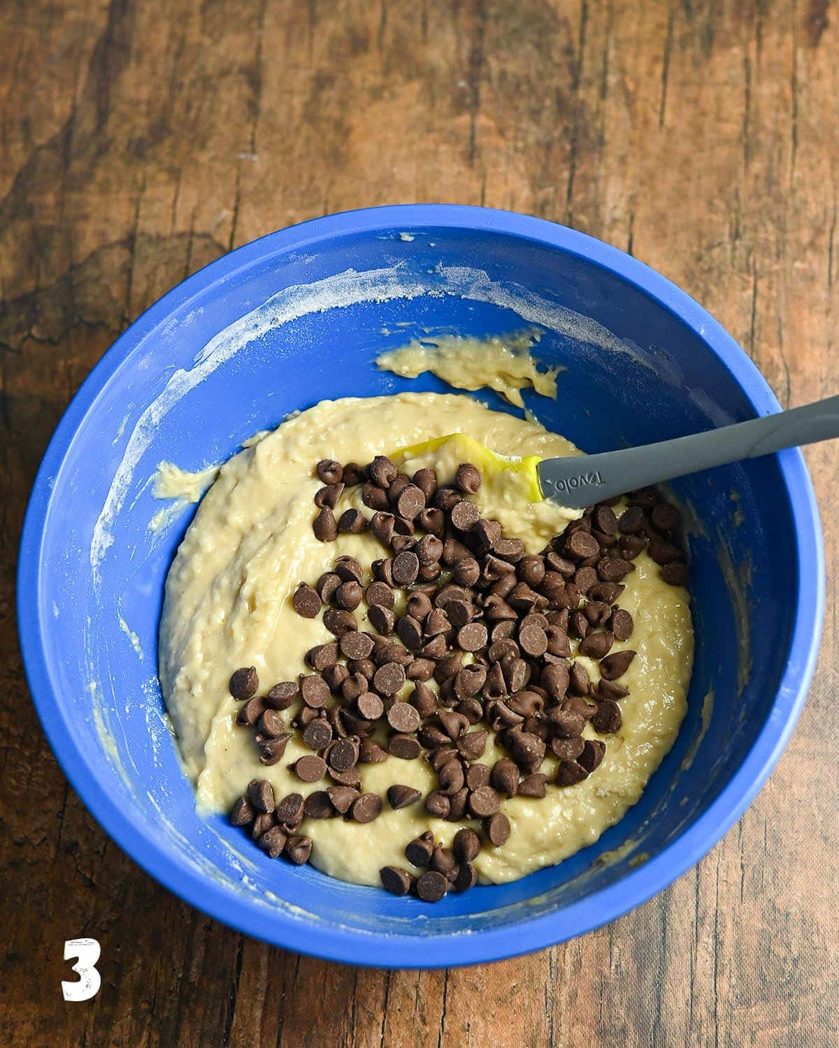 Chocolate chips added to muffin batter in a blue bowl.