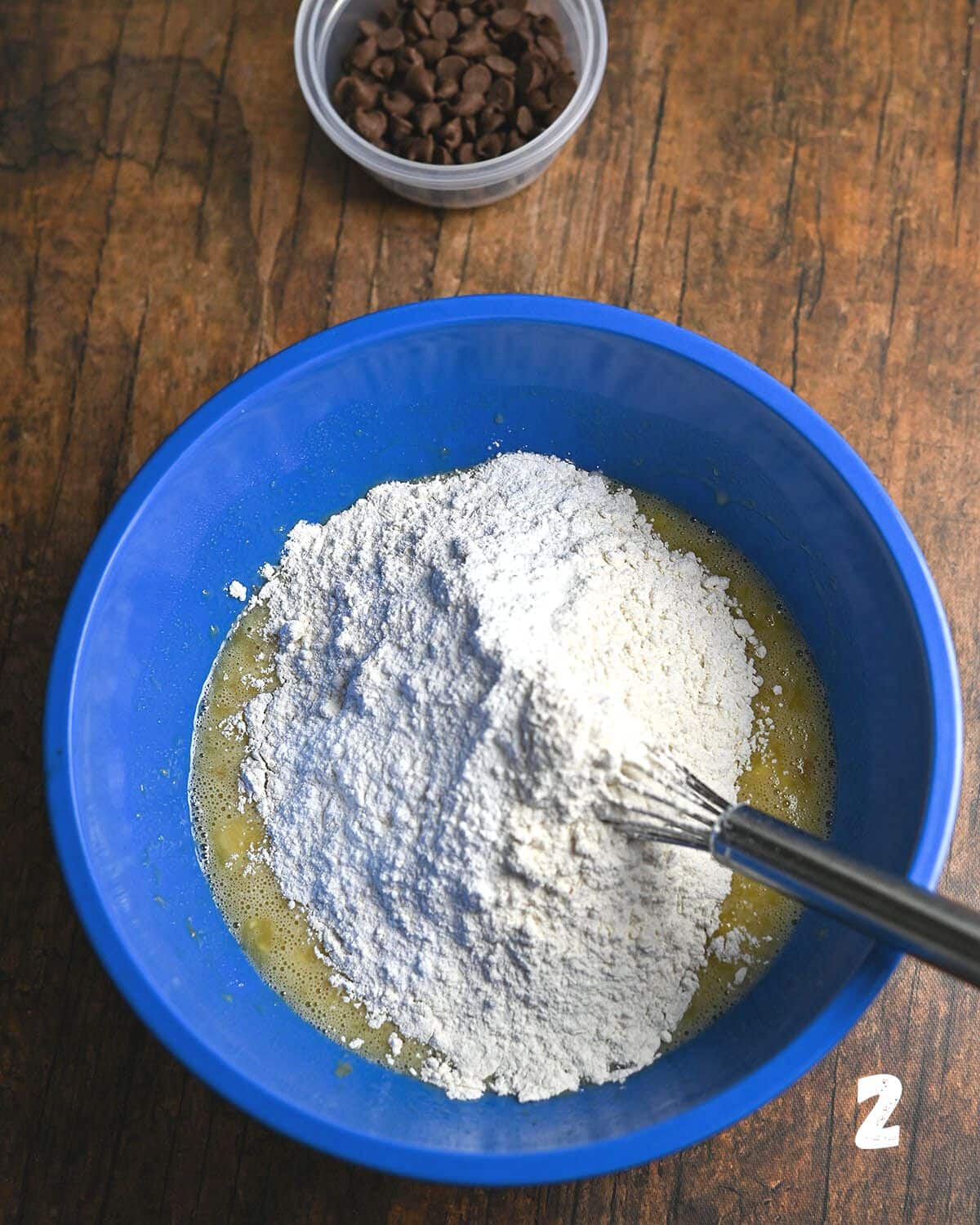 Dry ingredients over mixed wet ingredients to make muffins in a blue bowl.