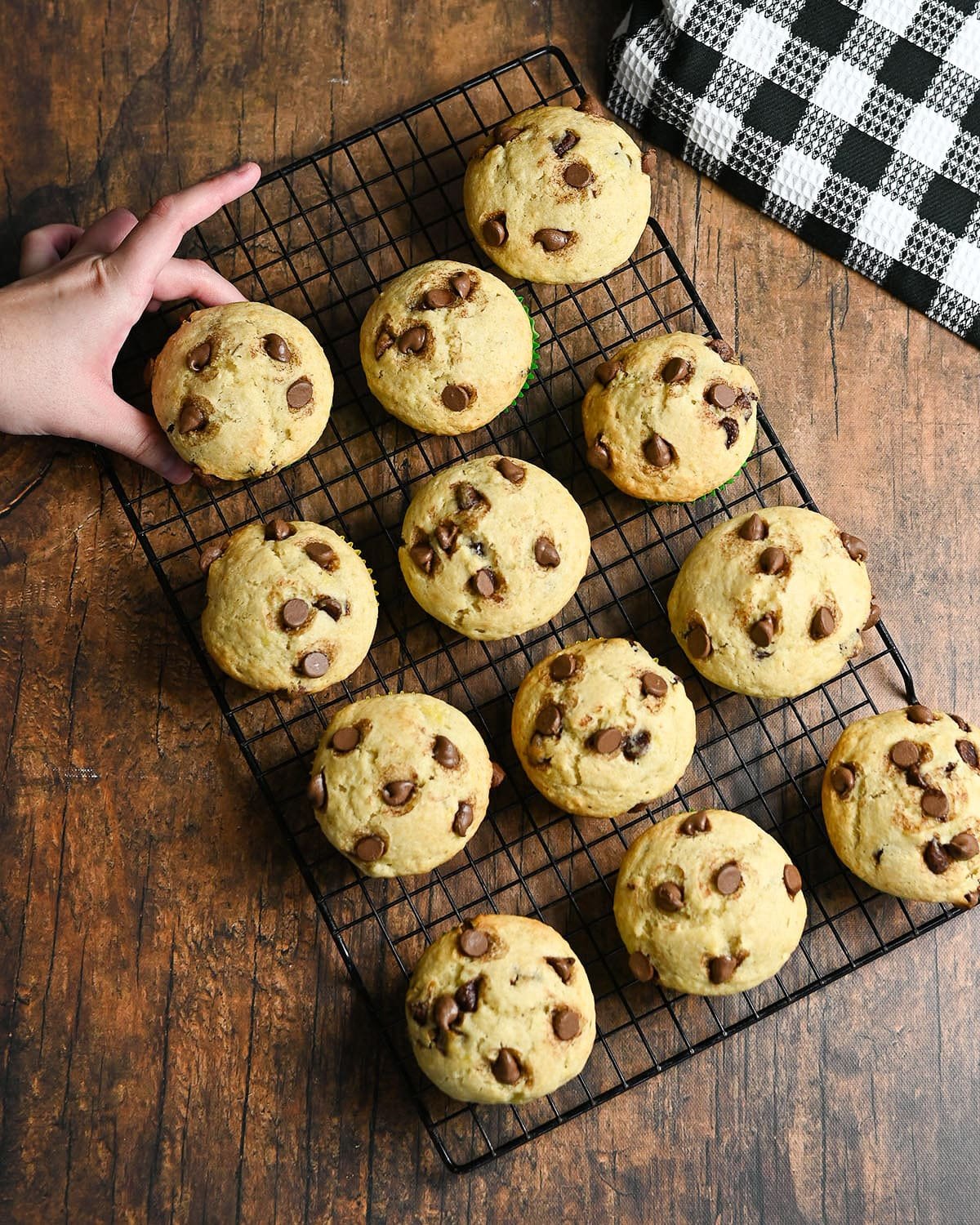 A hand grabbing a chocolate chip muffin off of a rack full of muffins. 