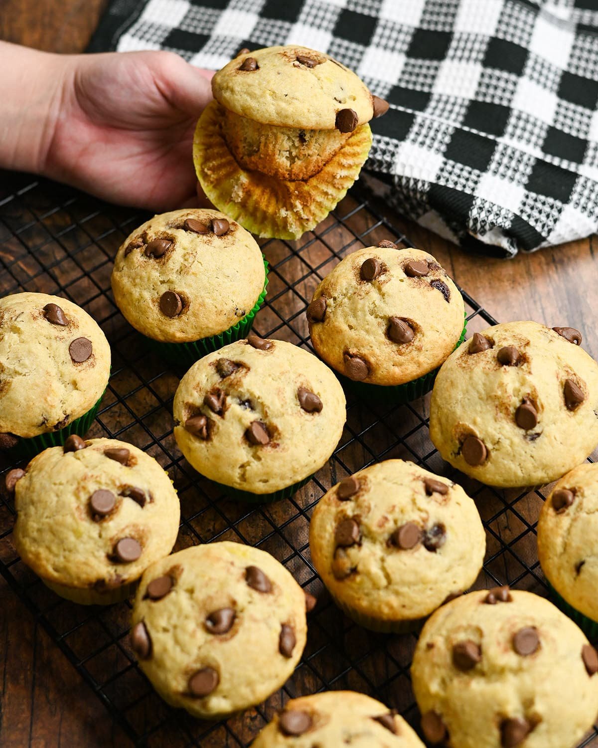 A wrapper partially removed from a chocolate chip muffin next to a rack of muffins.