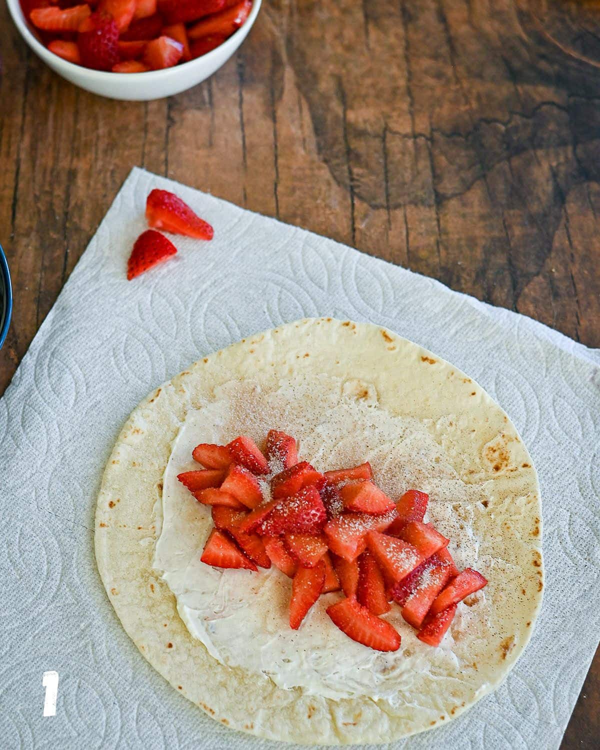 A tortilla with cream cheese and strawberries on it. 