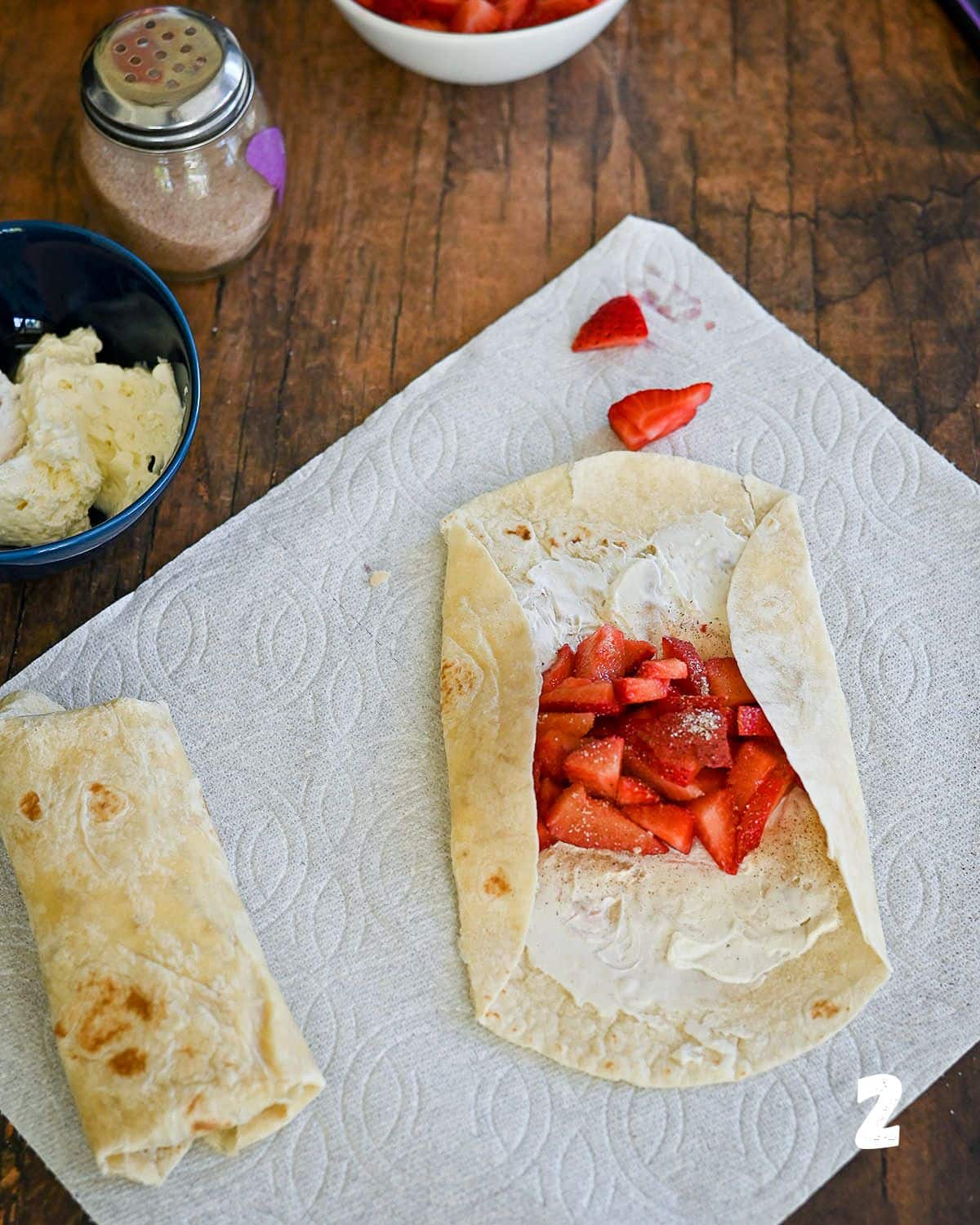 A strawberry filled tortilla being folded to make a burrito.