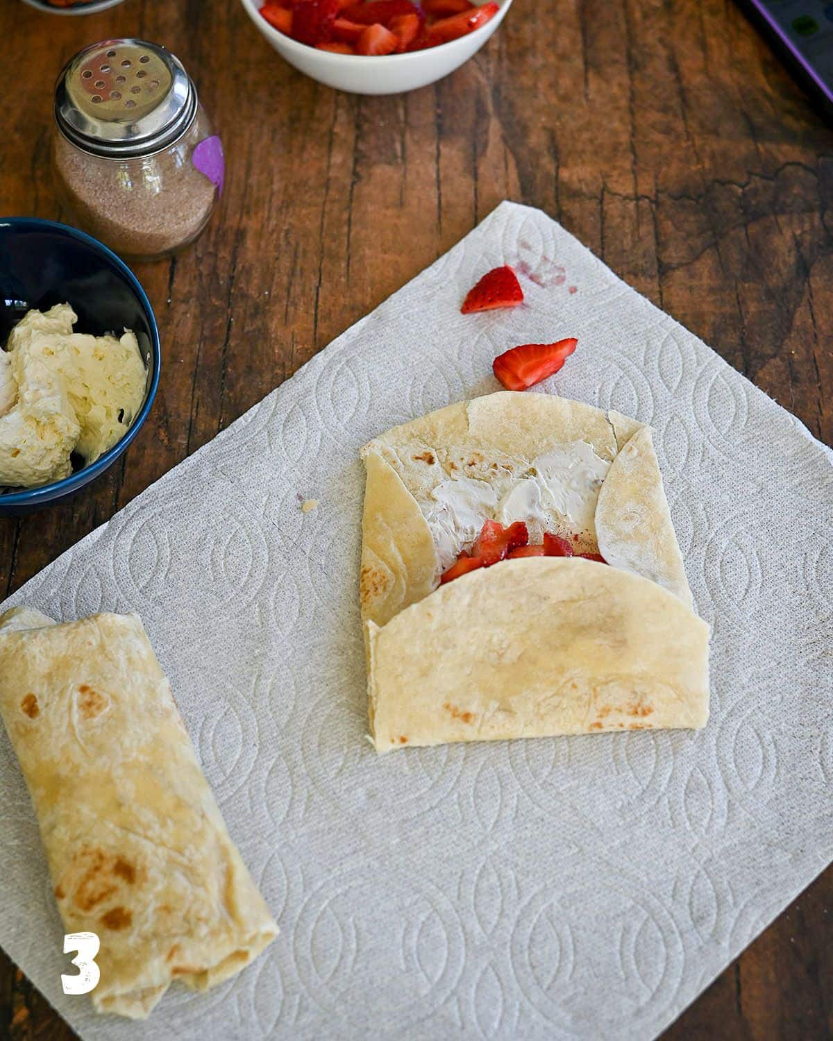 Folding a tortilla shell filled with cream cheese and strawberries.