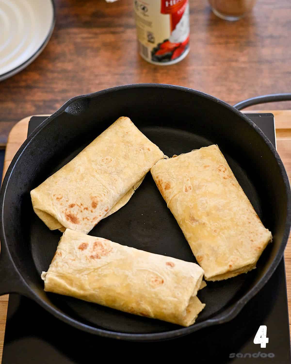 Stuffed tortilla shells cooking in a cast iron pan.