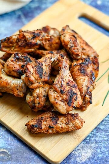 Grilled chicken wings on a board next to some chives and rosemary.