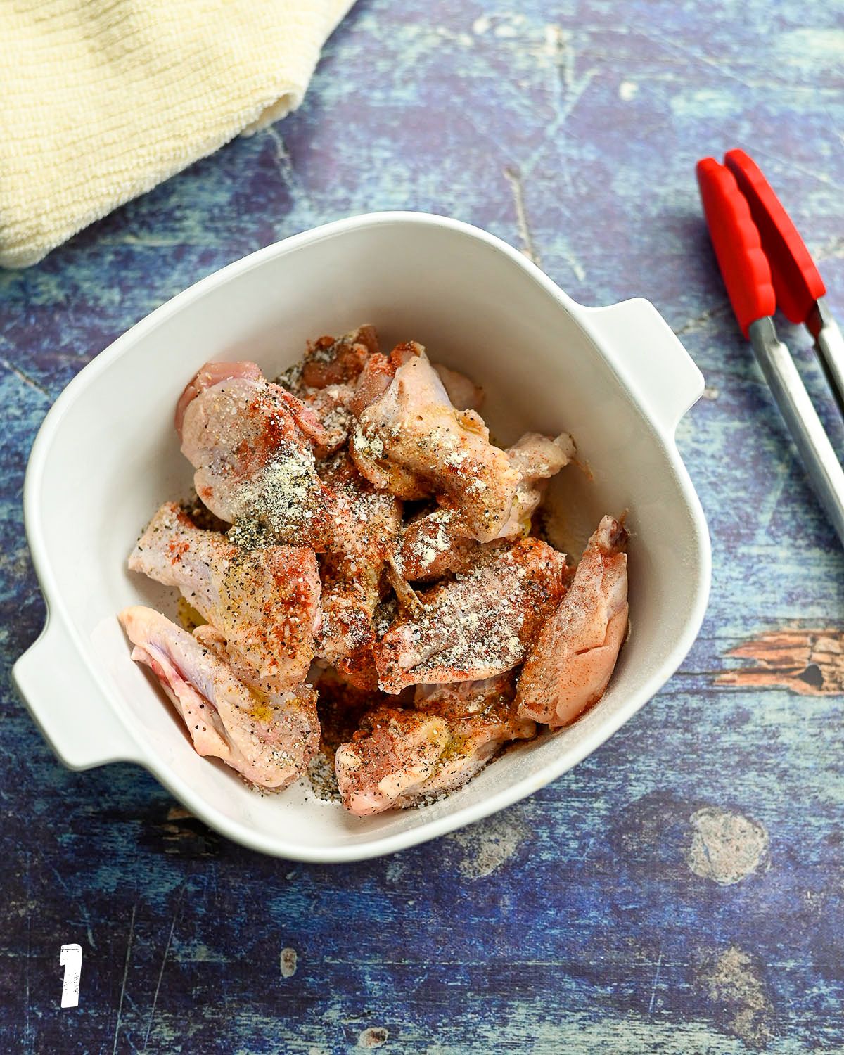 Raw chicken wings in a white bowl with oil and seasoning.