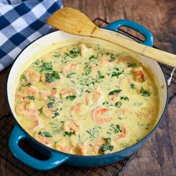 A large skillet with shrimp, coconut milk, and basil ready to eat.