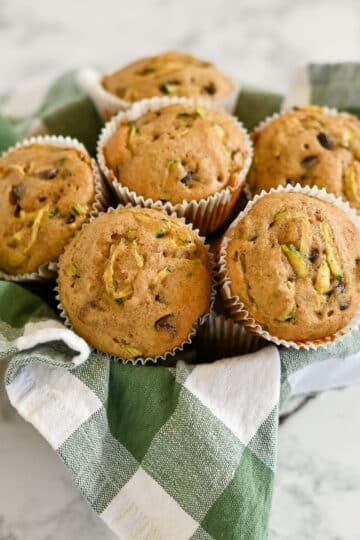 Basket of six Zucchini Bread Muffins with chocolate chips, made with applesauce and set on a green and white checkered cloth.