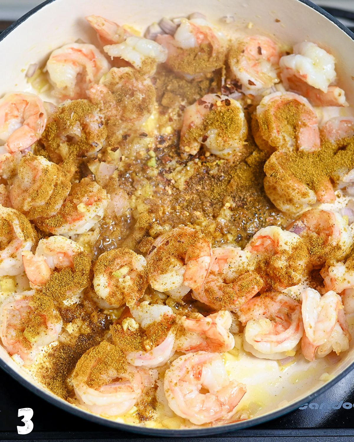 Curry powder being added to shrimp while cooking in a skillet.