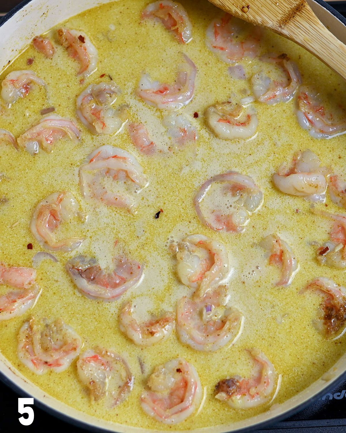 Coconut milk and broth added to shrimp cooking in a skillet.