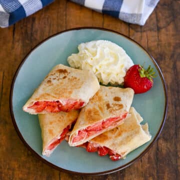 Strawberry burritos cut in half on a plate with whipped cream.