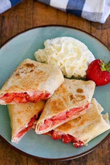 Strawberry burritos cut in half on a plate with whipped cream.