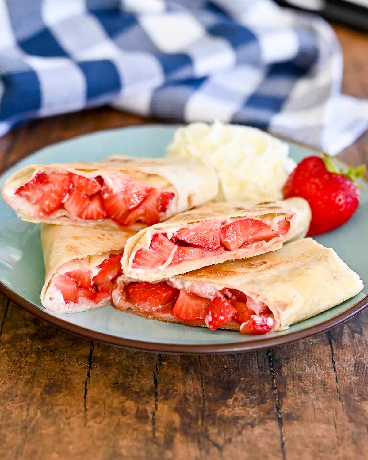 Tortillas filled with strawberries sitting on a blue green plate with whipped cream.