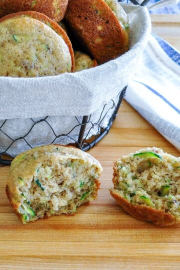 A split open zucchini muffin setting next to a basket of muffins.