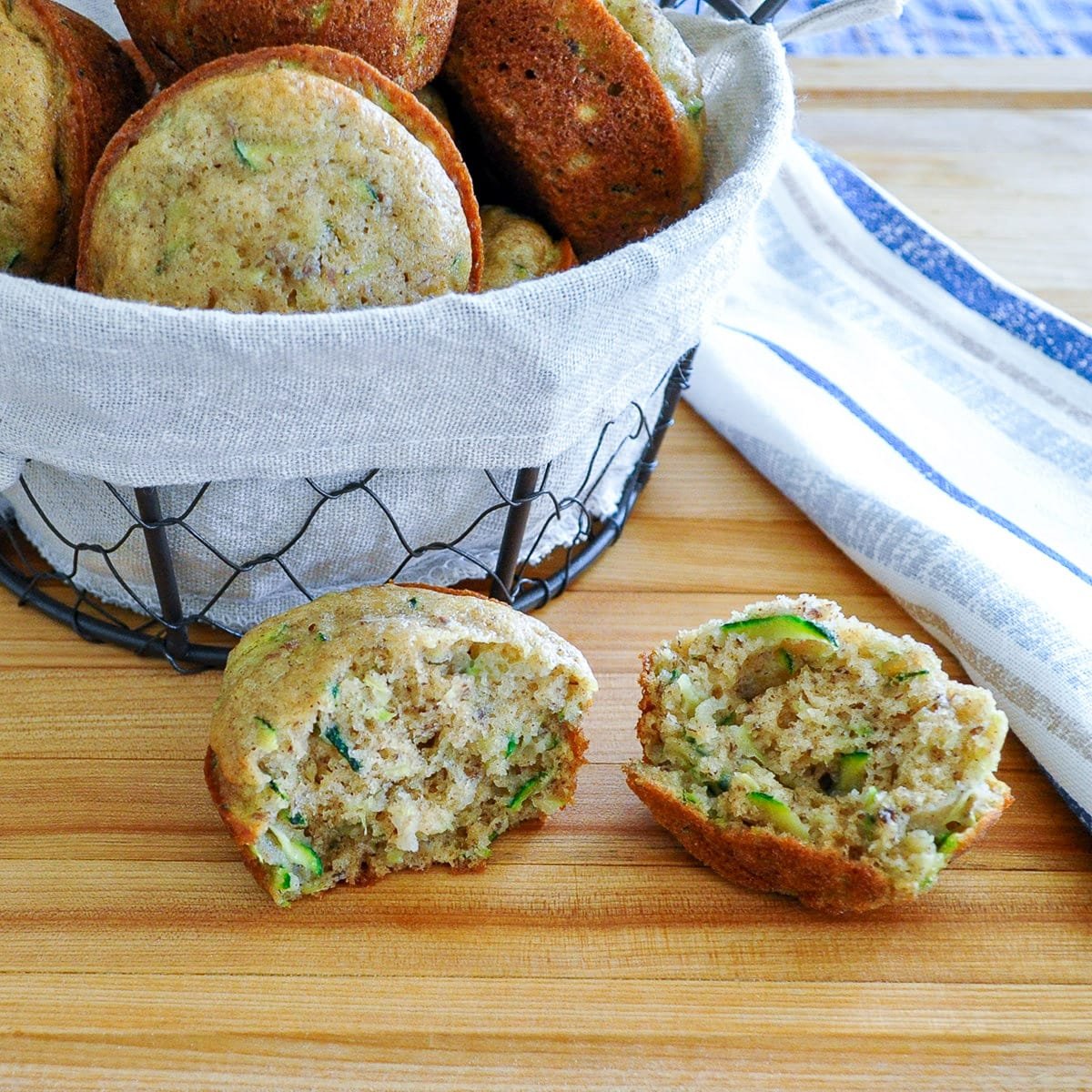A split open zucchini muffin setting next to a basket of muffins.