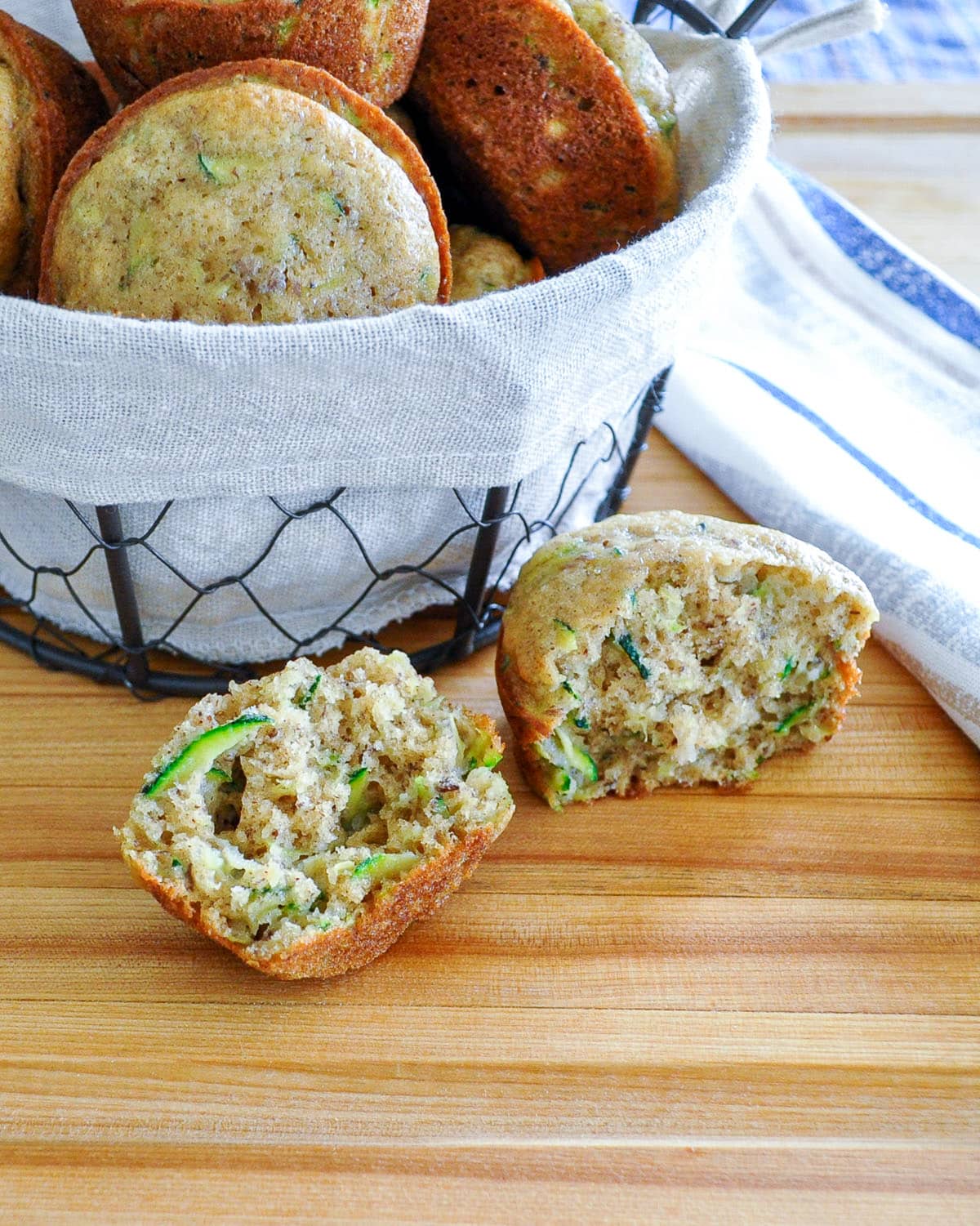 A split open zucchini muffin setting next to a basket of muffins. 