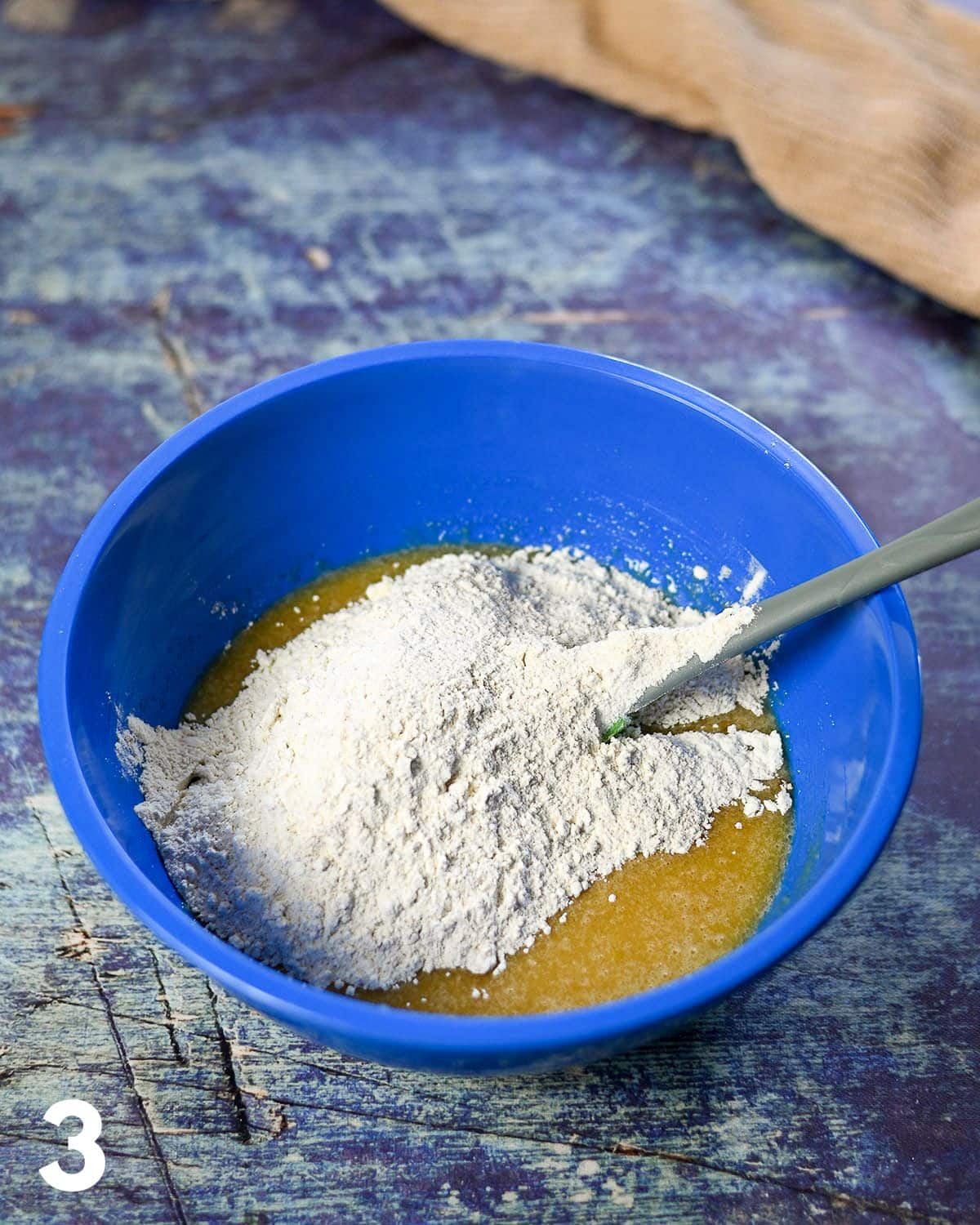 Mixing together dry and wet ingredients in a large blue bowl for cake.