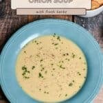 A blue bowl of homemade cream of onion soup with herbs sits next to crackers on a wooden table, inviting you to discover how to make cream of onion soup with simple, delicious ingredients.