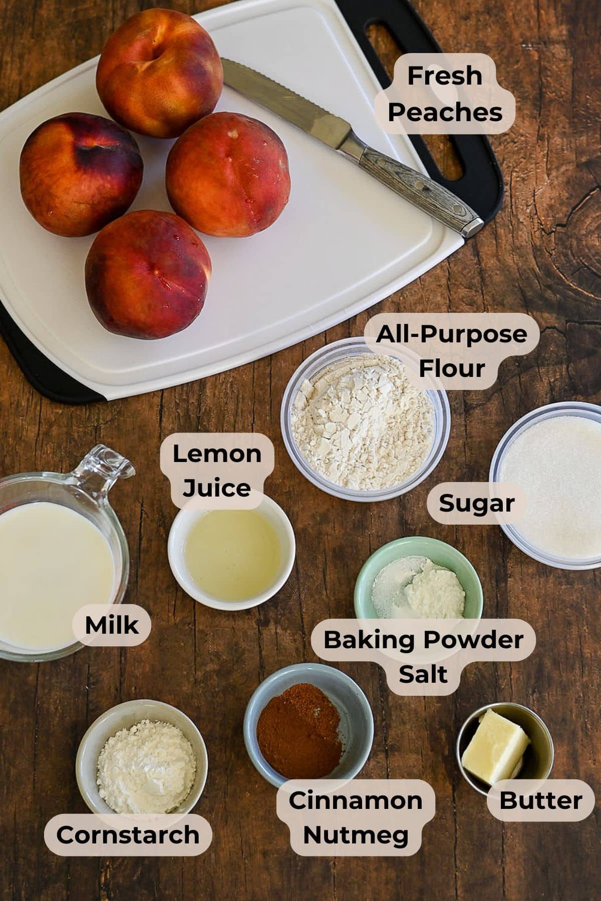 Fresh Peach Cobbler ingredients-fresh peaches, flour, sugar, milk, lemon juice, cornstarch, spices, butter, baking powder, and salt-arranged on a table.