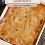 Fresh Peach Cobbler in a white dish on a cooling rack, featuring a golden-brown crust.