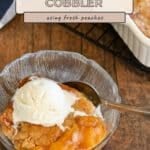A bowl of Fresh Peach Cobbler topped with vanilla ice cream sits next to a baking dish, a spoon resting in the bowl.