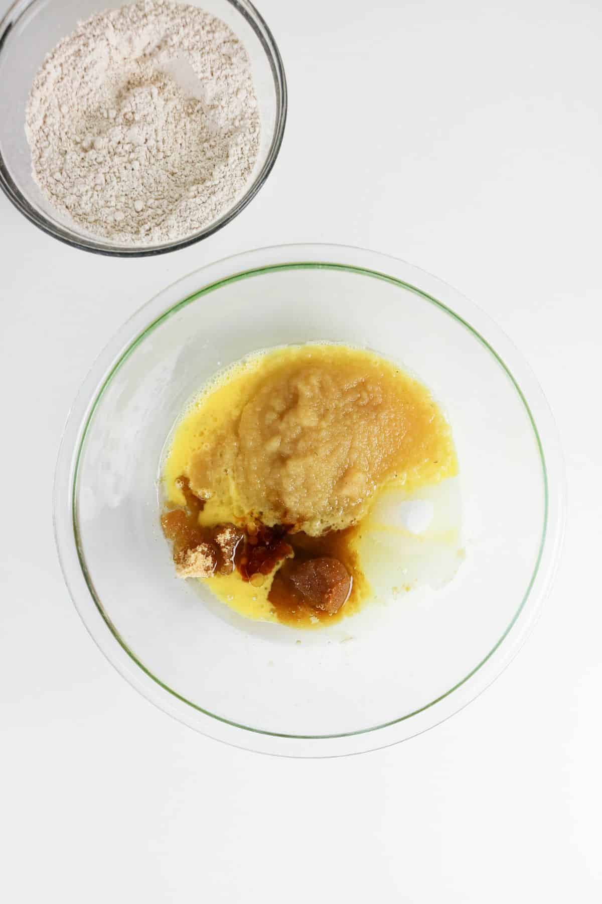 Two bowls: one with dry ingredients, the other brimming with applesauce, melted butter, and other wet ingredients.