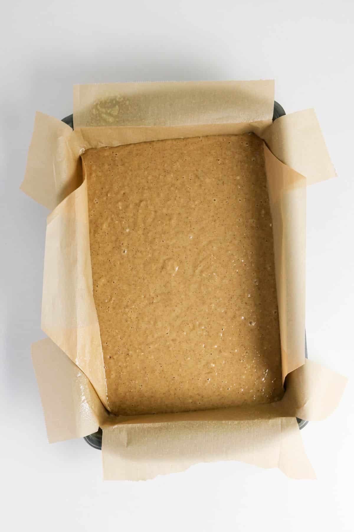 A baking pan lined with parchment paper filled with light brown Old-fashioned applesauce cake batter, ready to be baked.