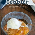 A bowl of Fresh Peach Cobbler topped with vanilla ice cream sits invitingly on a wooden table, with text overlay: "Peach Cobbler Using Fresh Peaches.