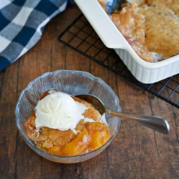 A clear glass bowl with peach cobbler and ice cream next to the dish of cobbler.