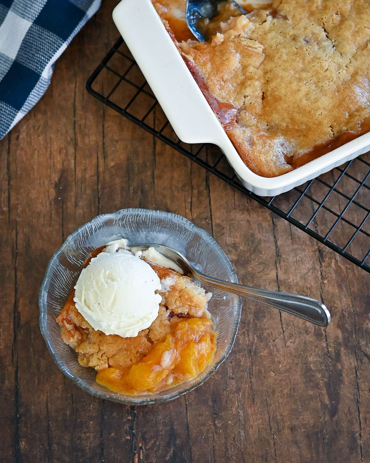 A clean glass bowl with peach cobbler and ice cream next to the dish of cobbler. 
