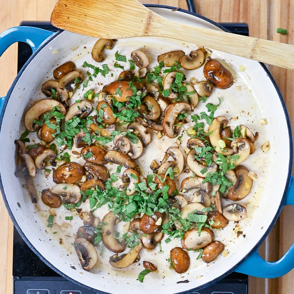 Fresh herbs added to mushroom cooking in a skillet.