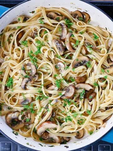 Pasta and herbs with mushrooms in a skillet.